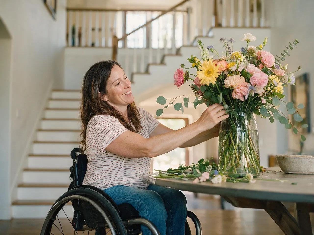 A woman arranging flowers in the bright entry hall of a large home